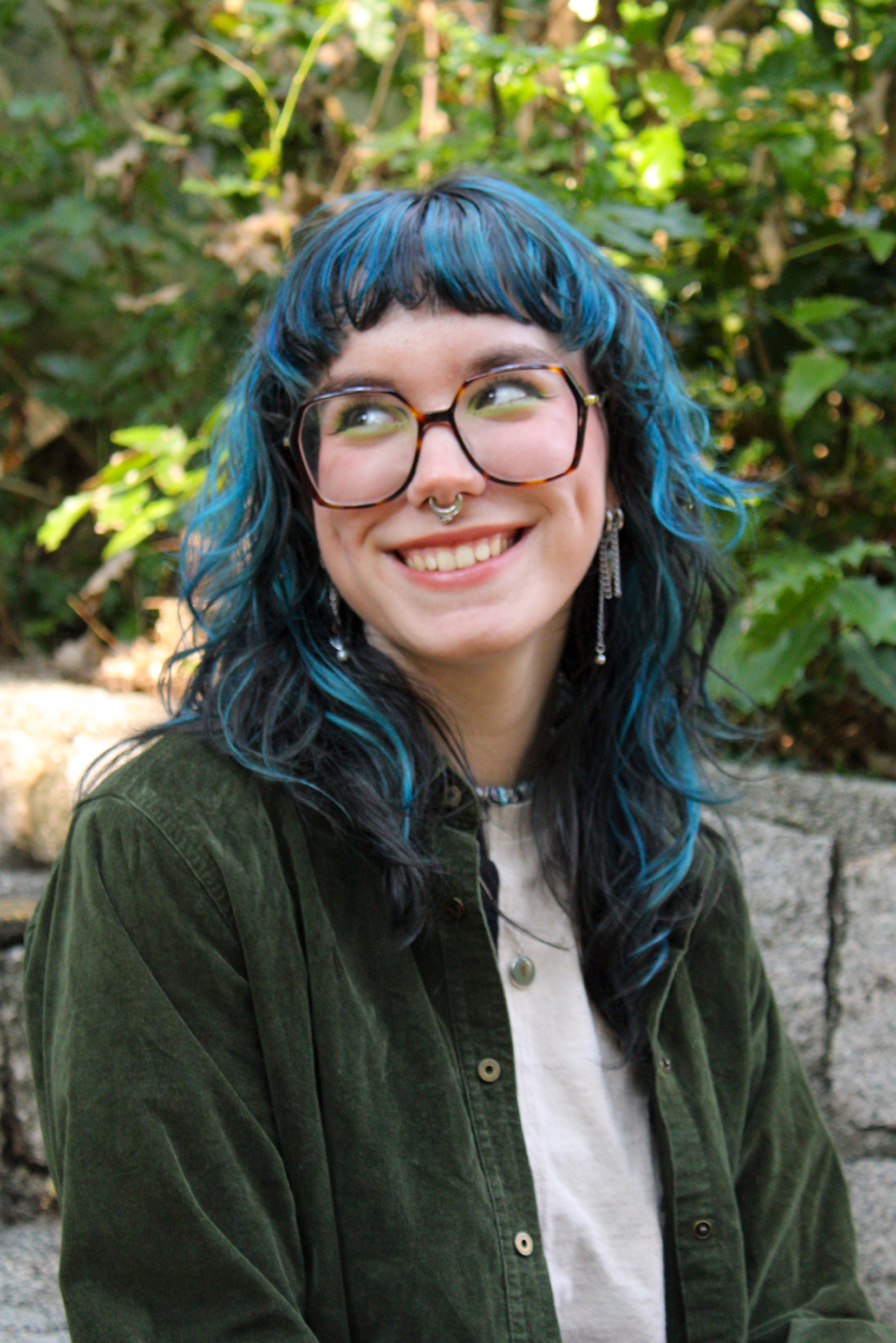 A photo of Lily Rosen, a young woman with blue hair and glasses smiling and glancing off-camera.